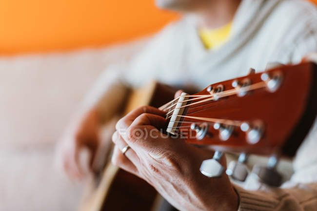 Nahaufnahme eines Mannes, der auf orangefarbenem Hintergrund Gitarre spielt — Stockfoto