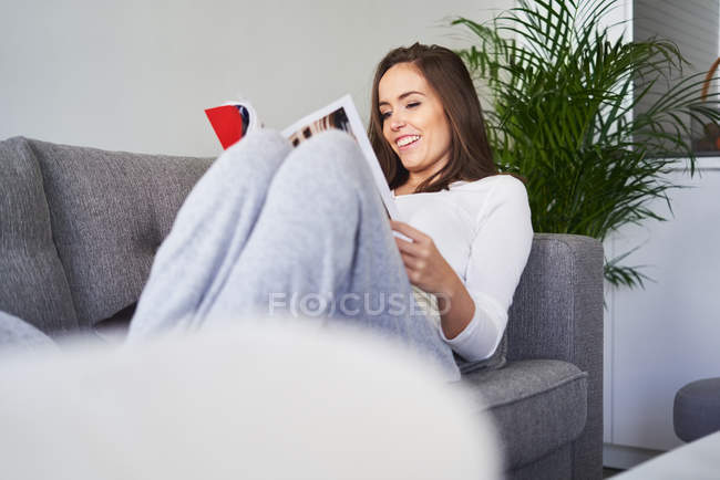 Щаслива жінка читає і відпочиває на дивані вдома. — стокове фото