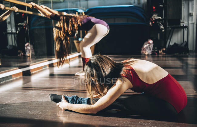 Vue latérale des ballerines s'échauffant et s'étirant dans un studio de ballet lumineux. — Photo de stock