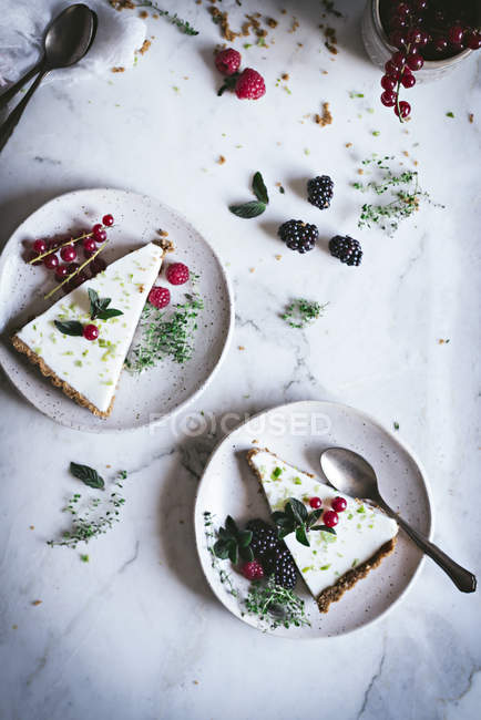 Pezzi di torta di lime con bacche fresche su piatti su superficie di marmo bianco — Foto stock