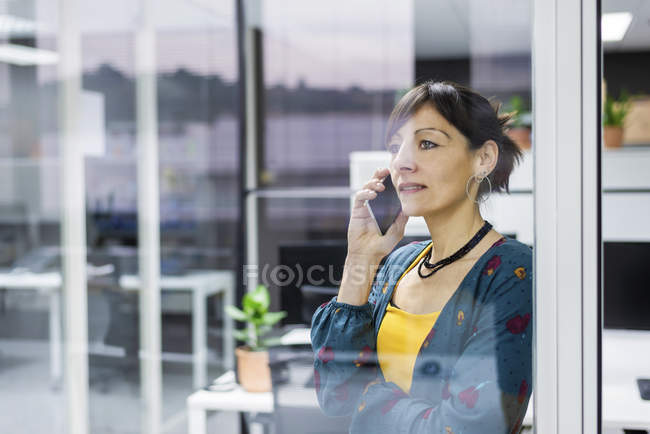 Female manager talking on mobile phone while standing near glass wall in modern office — Stock Photo