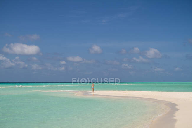 Vista posteriore della signora lontana in piedi sulla spiaggia sabbiosa vicino al meraviglioso mare turchese nella giornata nuvolosa alle Maldive — Foto stock