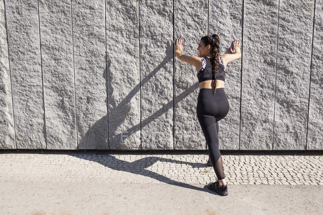 Brünette Frau dehnt an sonnigem Morgen ihre Muskeln gegen Betonwand — Stockfoto