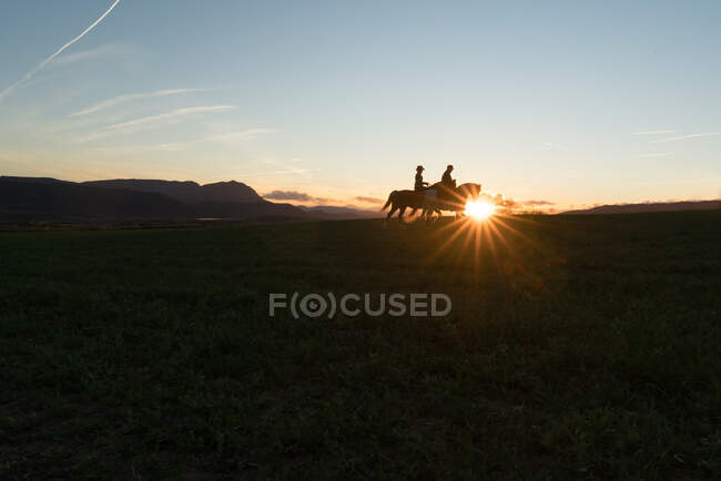 Mann und Frau reiten auf Ranch gegen den Sonnenuntergang — Stockfoto