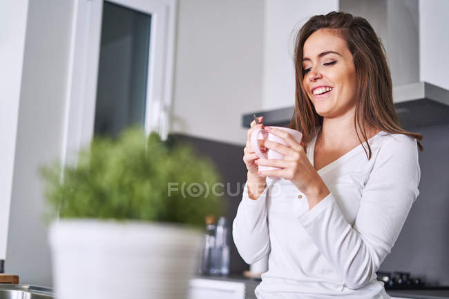Fröhliche junge Frau hält Tasse in moderner Küche zu Hause — Stockfoto