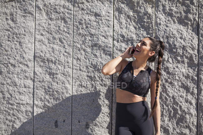 Donna bruna appoggiata al muro di granito mentre parla al telefono e ride — Foto stock