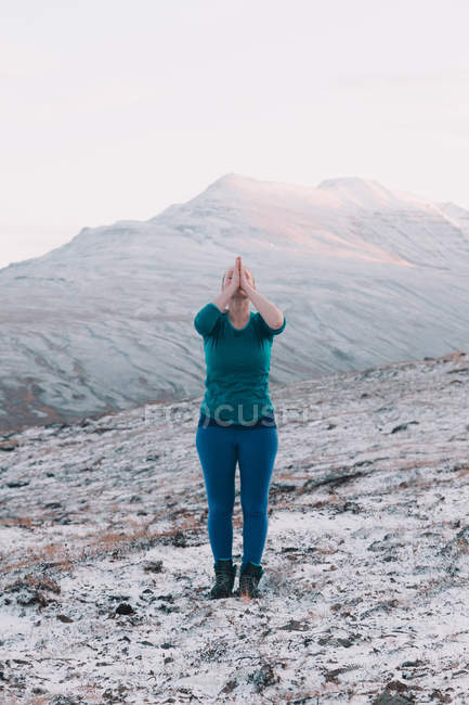 Mujer con las manos rezando meditando en las montañas nevadas - foto de stock