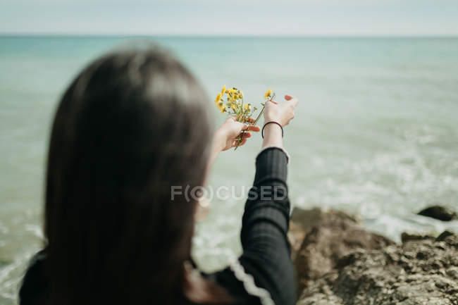 Руки женщины бросают маленькие желтые цветы в морскую воду в солнечный день — стоковое фото