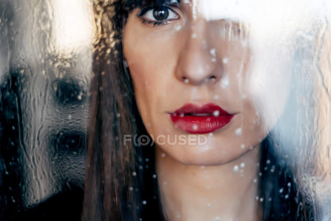 Attraktive Frau mit roten Lippen küsst hinter transparentem Glas — Stockfoto