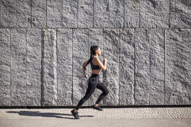 Brünette Frau läuft am sonnigen Morgen mit Granitmauer im Hintergrund — Stockfoto