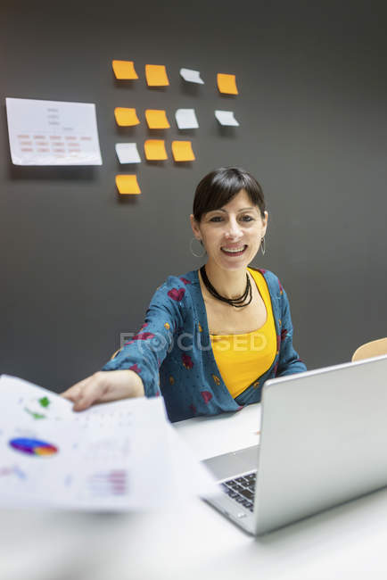 Sorridente empresária dando papéis com gráficos enquanto sentado na mesa no escritório moderno — Fotografia de Stock