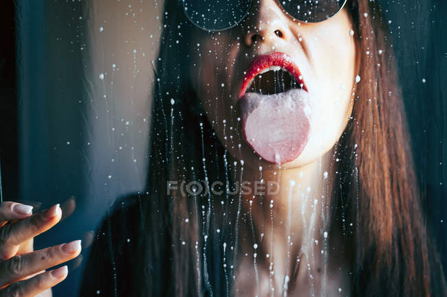 Attraktive Frau mit rotem Lippenstift leckt Flüssigkeitstropfen aus transparentem Glas — Stockfoto