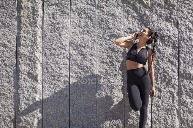 Брюнетка жінка спирається на гранітну стіну під час розмови по телефону і сміху — стокове фото