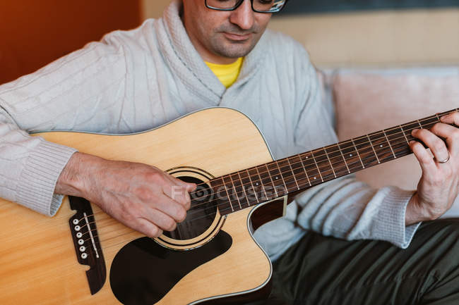 Nahaufnahme eines Mannes, der zu Hause auf dem Sofa Gitarre spielt — Stockfoto