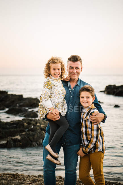 Homem de meia idade com seus filhos na costa do mar sorrindo e abraçando uns aos outros — Fotografia de Stock