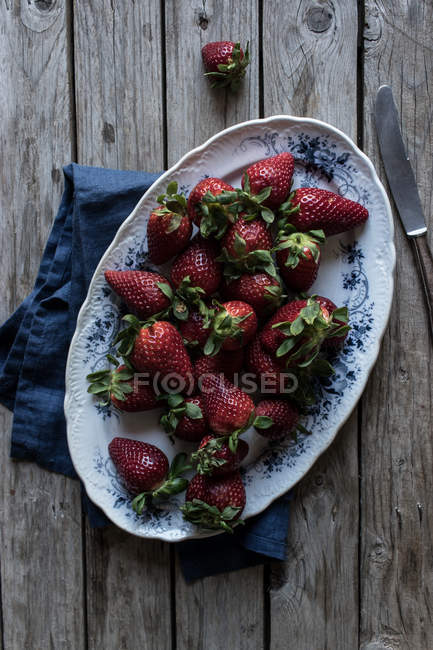 Placa de deliciosas fresas maduras sobre mesa de madera cerca de servilleta azul y cuchillo de metal - foto de stock