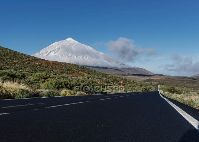 Route de campagne asphaltée à travers un terrain herbeux près d'un magnifique sommet enneigé par temps ensoleillé sur les îles Canaries, Espagne — Photo de stock