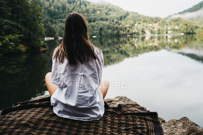 Woman sitting on blanket near lake and mountains — Stock Photo