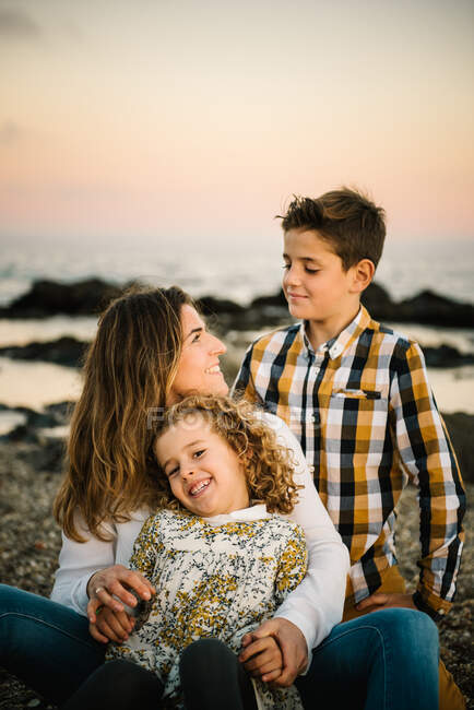 Женщина средних лет с детьми на берегу моря улыбается и обнимает друг друга — стоковое фото
