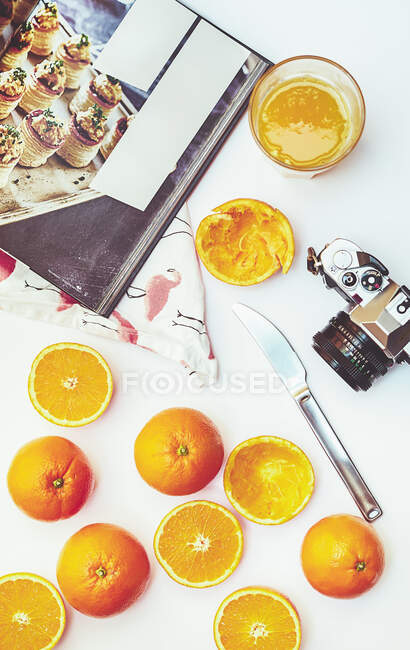 Colocação plana de laranjas inteiras e cortadas pela metade com livro de culinária e câmera fotográfica vintage na mesa branca — Fotografia de Stock