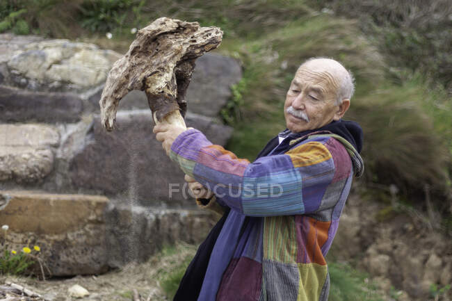 У віці чоловік в куртці ламає грубий кам'яний шматок, що стоїть на узбережжі — стокове фото