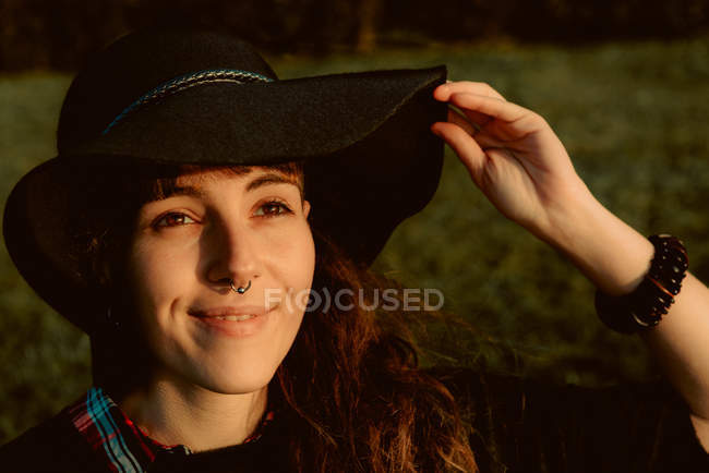 Jovem morena sensual vestindo chapéu preto e acessórios enquanto posando à luz do sol — Fotografia de Stock