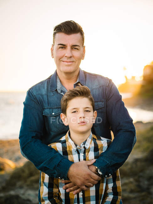 Uomo di mezza età con suo figlio sulla riva del mare che sorride e si abbraccia — Foto stock