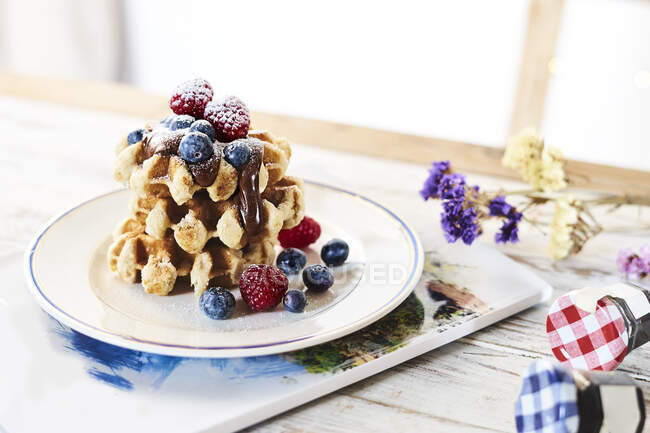 Prato com pilha de waffles dourados decorados com bagas frescas e cobertura de chocolate na mesa — Fotografia de Stock