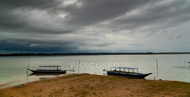 Barche tradizionali sulla spiaggia di sabbia con acque calme sotto il cielo scuro nuvoloso, Cambogia — Foto stock