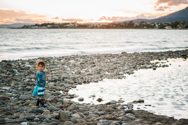 Linda niña pequeña jugando con piedras en la playa - foto de stock