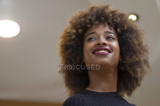 Усміхнений афроамериканець жінка з Кучеряве волосся дивиться геть проти стелі кімнати — стокове фото