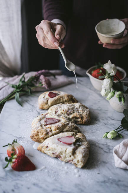 Pessoa irreconhecível adicionando molho de creme doce a scones de morango saborosos enquanto cozinha — Fotografia de Stock