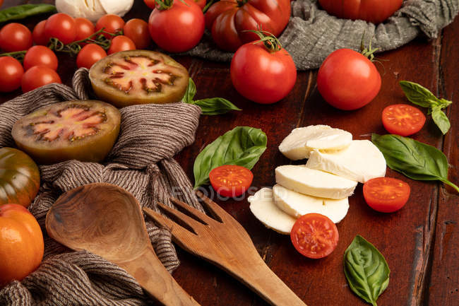 Fresh tomatoes and mozzarella cheese with basil leaves for salad on wooden surface and fabric napkin — Stock Photo