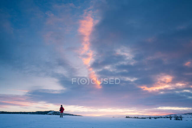 Турист у теплому одязі, що стоїть на величному засніженому полі на фоні яскравого неба заходу сонця — стокове фото