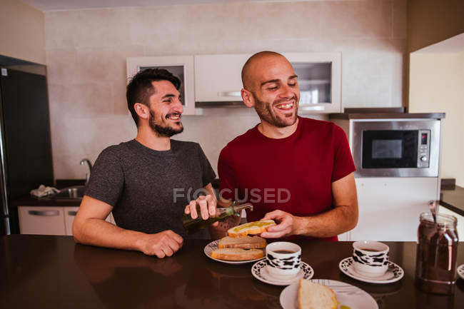 Alegre gay casal ter pequeno-almoço no cozinha no casa — Fotografia de Stock