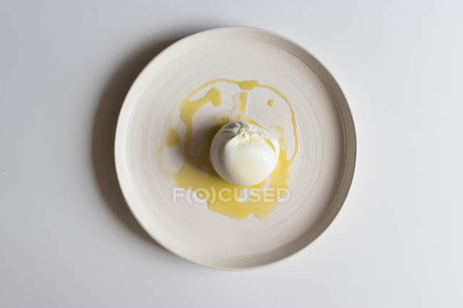 Шар вкусной бурраты с маслом на керамической пластине на белом фоне — стоковое фото