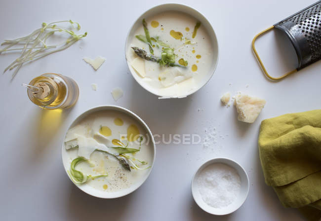 Bols de délicieuse soupe à la crème d'asperges avec du fromage et des herbes sur fond blanc — Photo de stock
