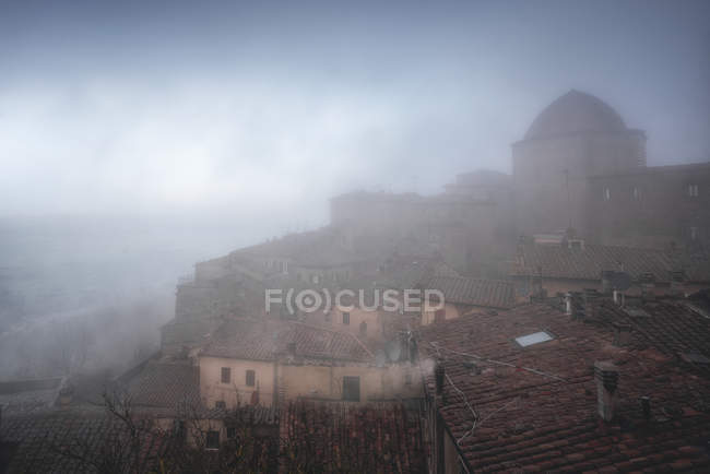 Екстер'єр старих червоних цегляних будівель міста Вольтерра проти туманного неба, Італія — стокове фото
