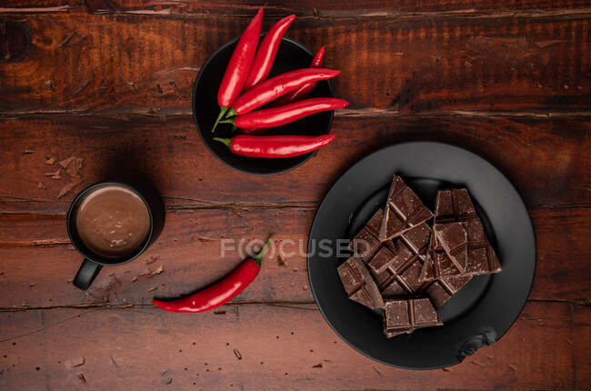 Tasse de boisson chaude fraîche placée sur une table de bois près d'une assiette avec des morceaux de chocolat et de piment — Photo de stock