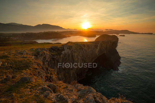 Panoramic view of huge rocky cliffs above rippled water against sunset sky, Asturias, Spain — Stock Photo