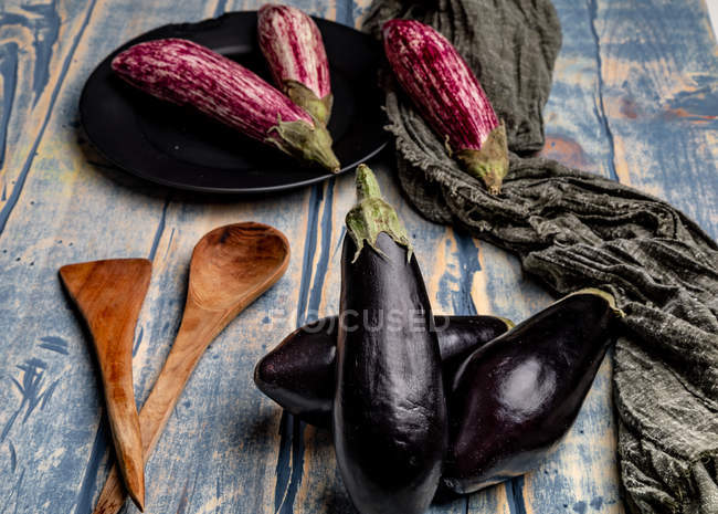 Berinjelas maduras frescas perto de pedaço de pano listrado na mesa de madeira intemperizada — Fotografia de Stock