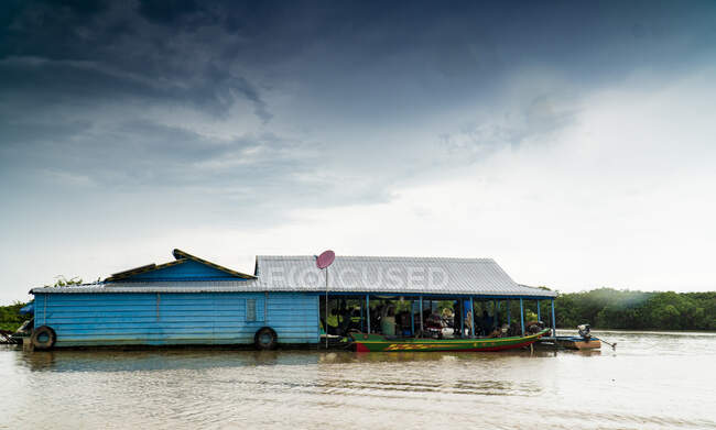 Pequeña casa flotando río abajo contra la vegetación tropical en la orilla, Camboya - foto de stock