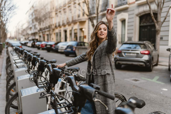 Elegante signorina che sceglie noleggio biciclette sul parcheggio e punta con il dito — Foto stock