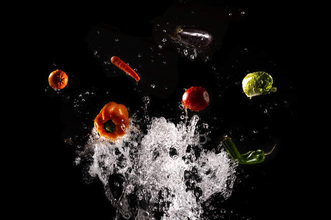 Schwebendes reifes Gemüse und Salat in klaren Wasserspritzern auf schwarzem Hintergrund — Stockfoto