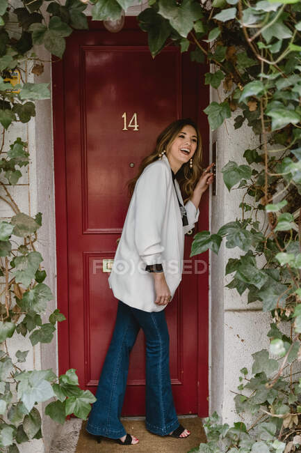 Stylische Frau steht vor roter Tür — Stockfoto
