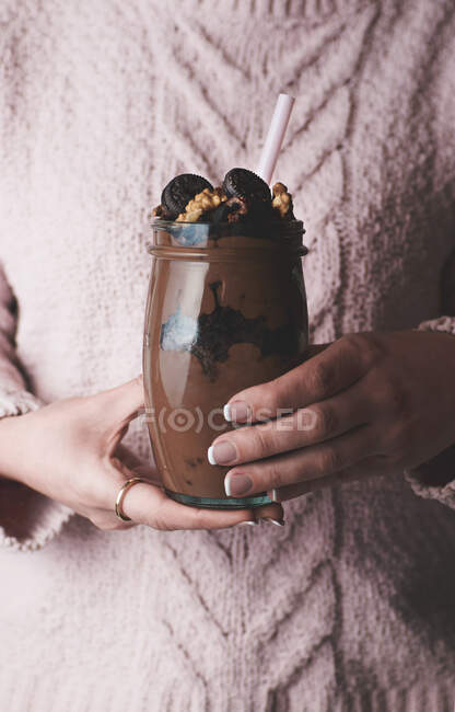 Безликая женщина в розовом свитере держит стакан шоколадного смузи с орехами и конфетками — стоковое фото