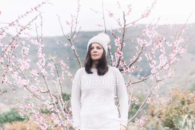 Pensive female in sweater and hat standing in spring countryside — Stock Photo
