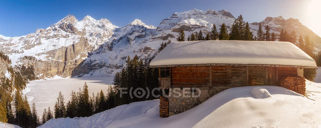 Vista panoramica del pendio innevato con casa in legno sullo sfondo delle montagne alla luce del sole, Svizzera — Foto stock