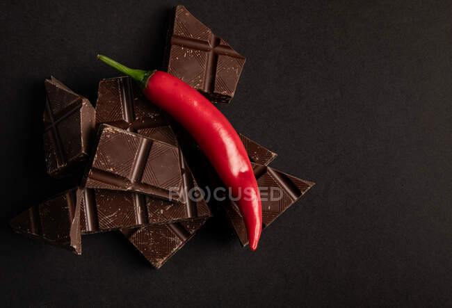 Pezzi di cioccolato gustoso posto con peperoncino su sfondo scuro — Foto stock