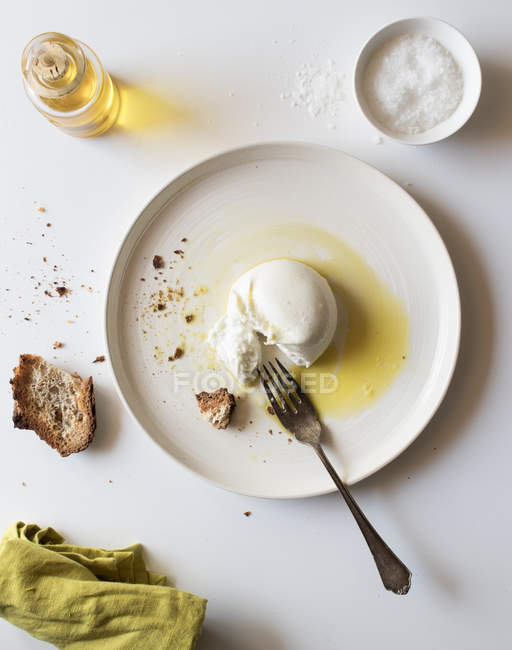 Prato com deliciosa burrata fresca na mesa branca perto de pedaço de pão e óleo com sal — Fotografia de Stock